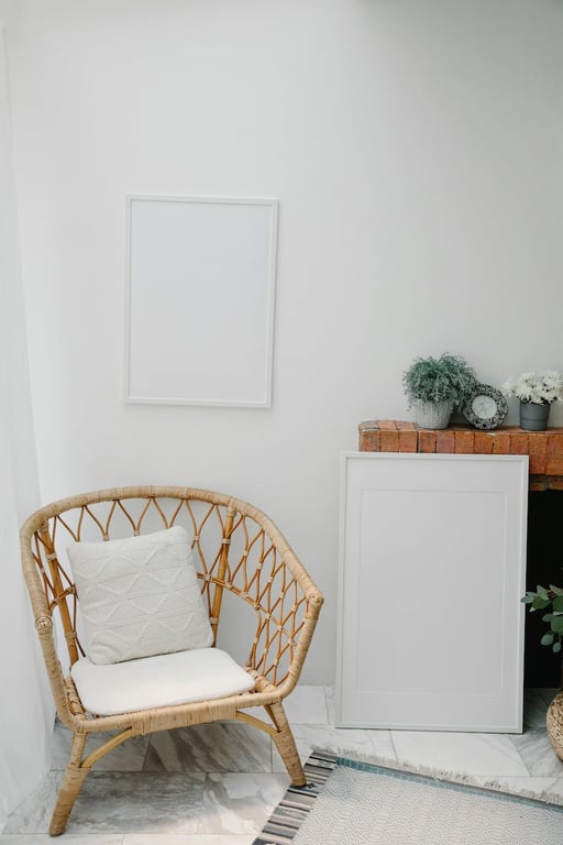 Fauteuil confortable avec coussins placé dans un coin sous un cadre blanc vide accroché près d'une étagère avec des plantes en pot